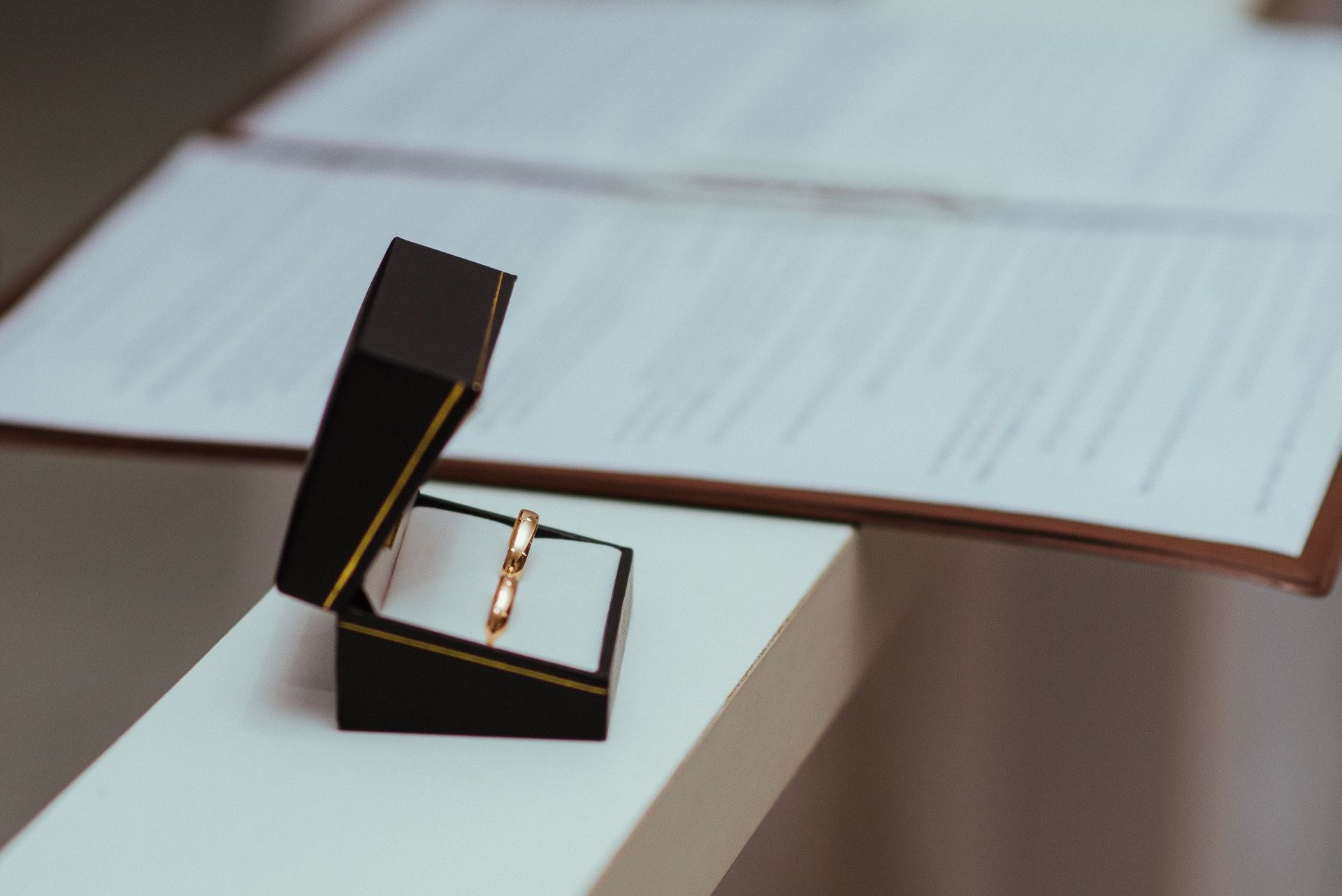 A pair of wedding rings in a black box next to important documents, symbolizing commitment.
